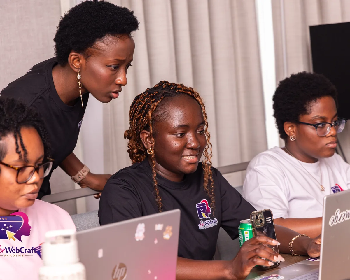A HerWebCraft instructor helping Cohort 1 students at their laptops