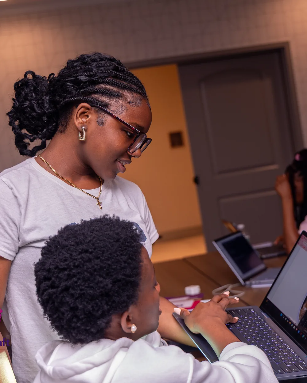 A smiling Cohort 1 student helping a classmate at her laptop